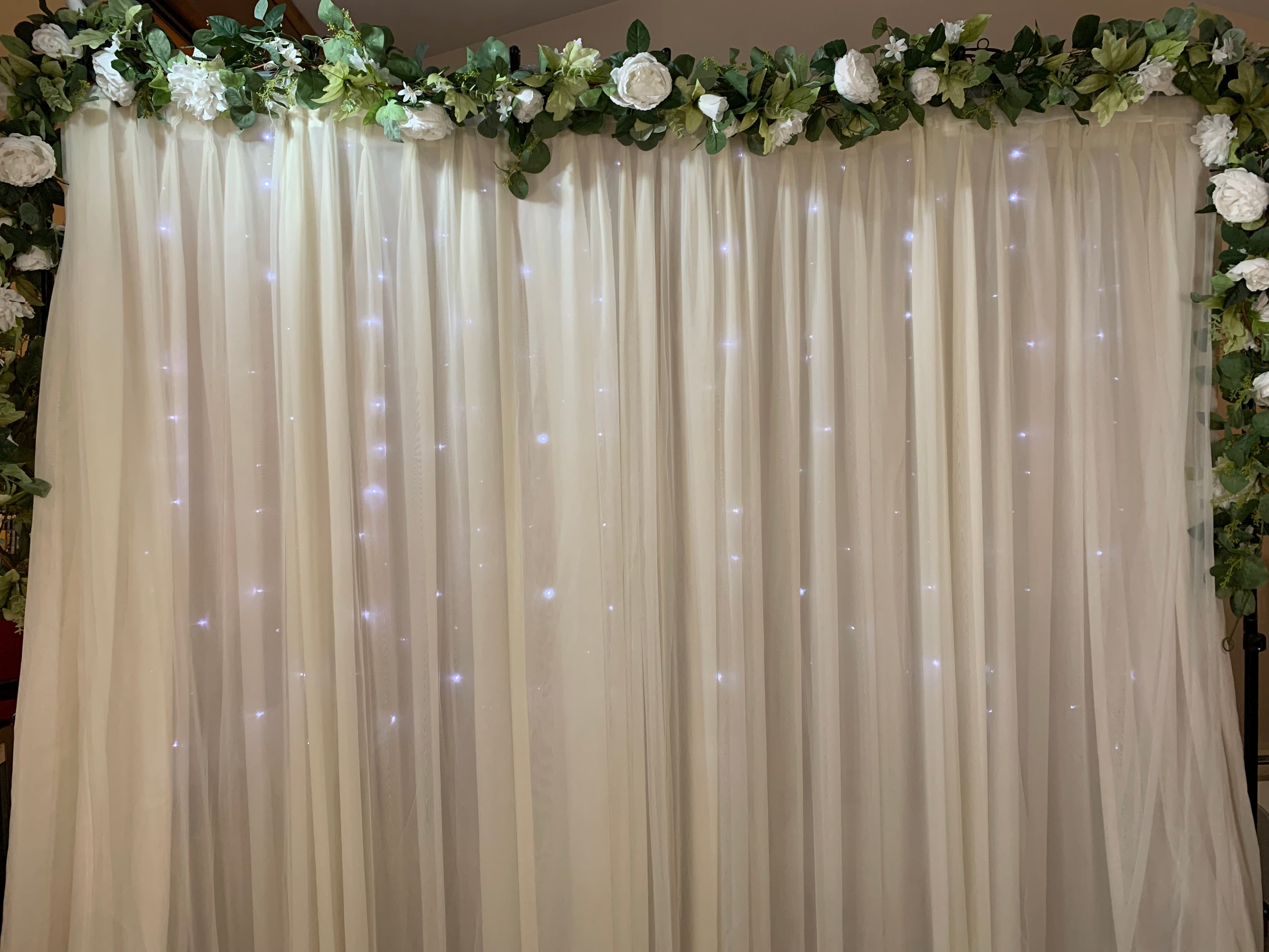 Beige backdrop with fairy lights and floral decorations at the top